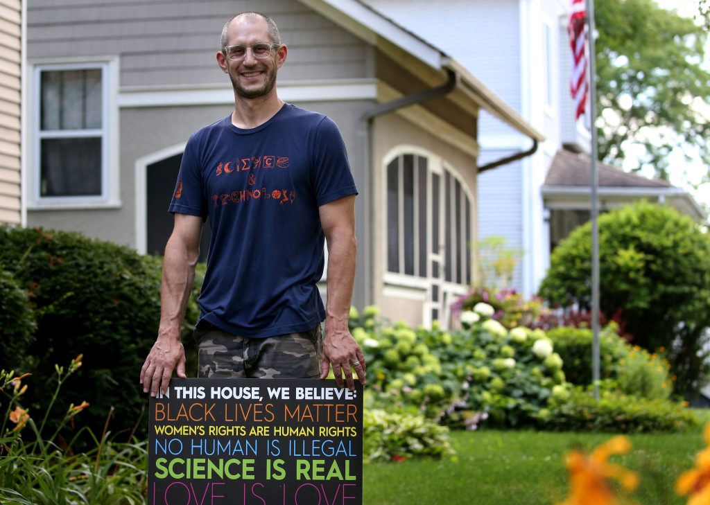 Aaron Podolner standing outdoors holding a sign supporting social justice and community